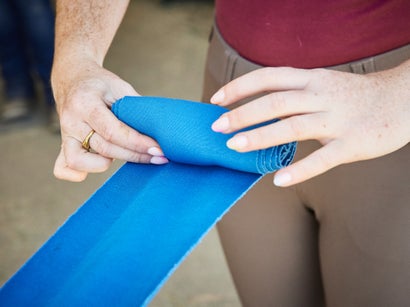 Pre-wrapping a blue stable bandage prior to putting it on a horse's leg. Continuing to roll into the velcro. 