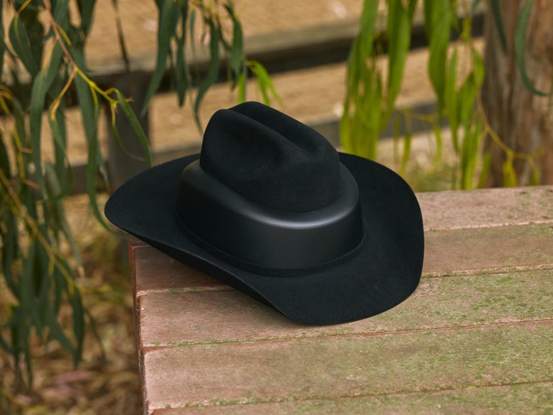 The Resistol RideSafe Western Felt Cowboy Hat Helmet sitting on a wooden picnic table