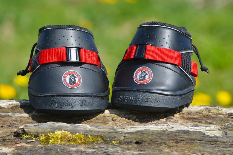 The Equine Fusion Ultra Jogging Shoe Hoof Boots sitting on a wooden log with green grass in the background. They are the best hoof boots for turnout, pasture, and riding. 