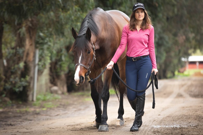 A rider wearing the Ariat Tri Factor Grip Full Seat Breeches hand walking her bay horse.