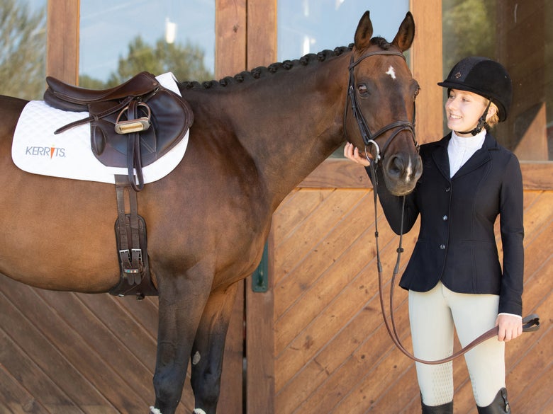 Woman standing next to her bay horse wearing the Kerrits Affinity Aero Show Coat. 