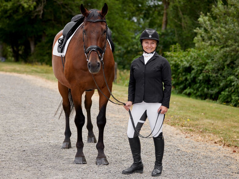 Woman standing with her bay horse wearing the Kerrits Stretch Competitor Koat Show Jacket in black.