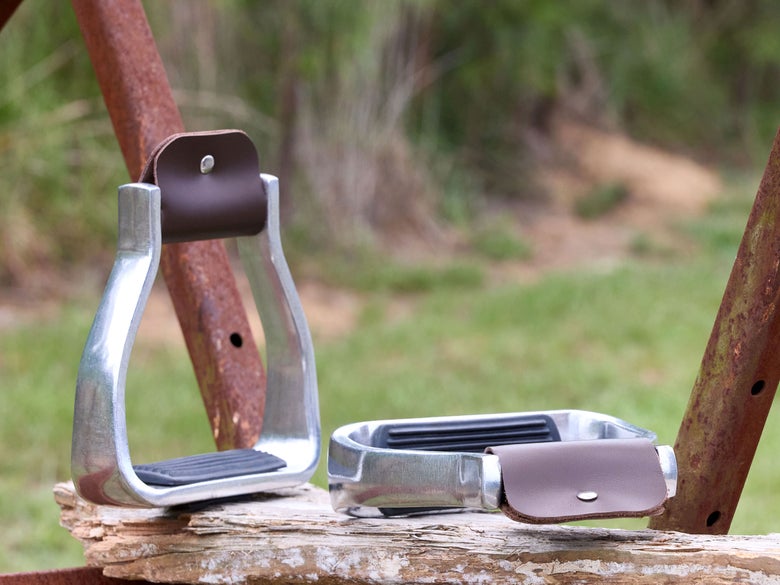 The Martin Saddlery Aluminum Western Stirrups sitting on a log next to a fence. 