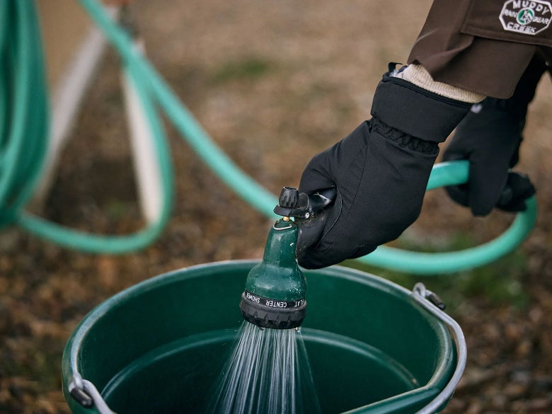 Equestrian filling up water bucket with hose while wearing the Mountain Horse Heat Waterproof Winter Gloves.