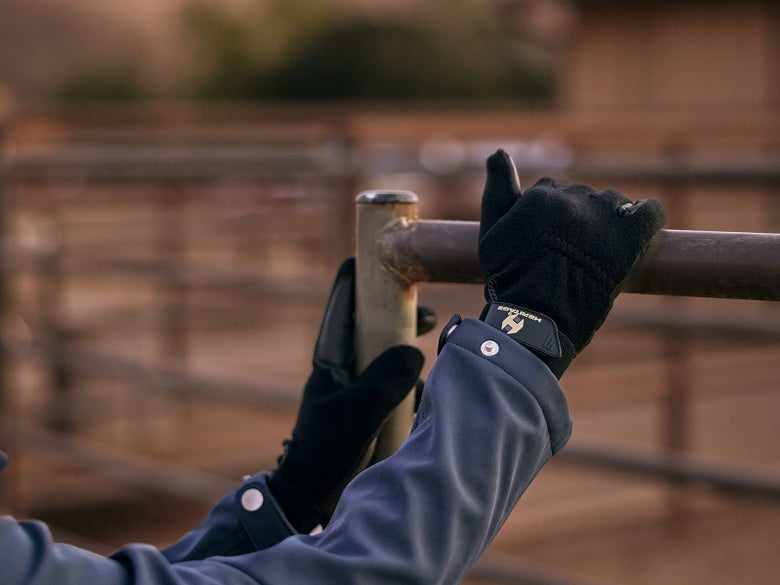 Rider with their hands on a brown metal railing, wearing the Heritage Performance Fleece Winter Riding Gloves.