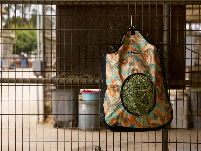 A weaver breathable easy fill hay bag hanging on a stall that is filled with bermuda hay.