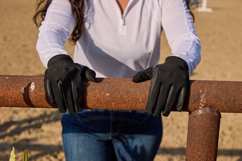 A rider wearing the Dublin Pull On Cool Mesh Riding Gloves with her hands on a railing.