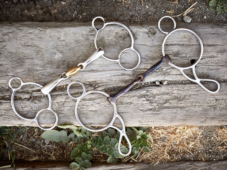 A horse bit with gag cheekpieces, laying flat on a piece of wood. 