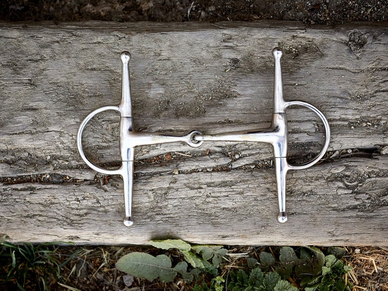 Image of a full-cheek horse bit sitting flat on a piece of wood. 