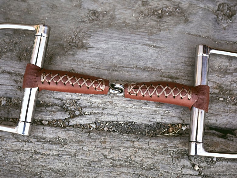 Close up image of a bit wrapped in leather, laying flat on a piece of wood. 