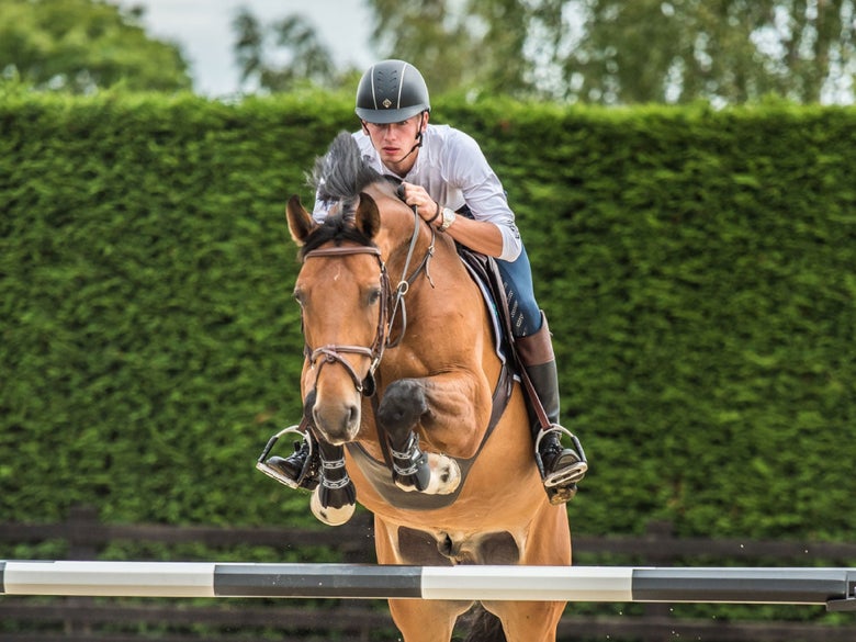 Man wearing a Charles Owen helmet riding over a jump on his bay horse