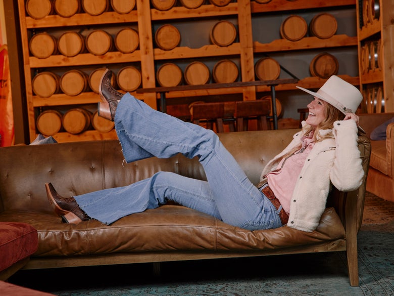 Girl laying on couch with a cute western style outfit on, kicking her feet up in the air wearing short cowboy boots