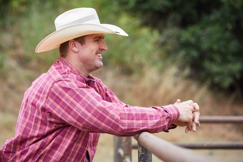 Man leaning over fence wearing a straw cowboy hat. 