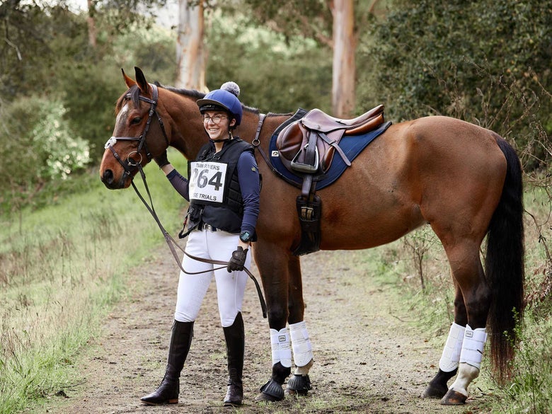 Bay horse and rider dressed in a navy blue and white cross country tack kit.