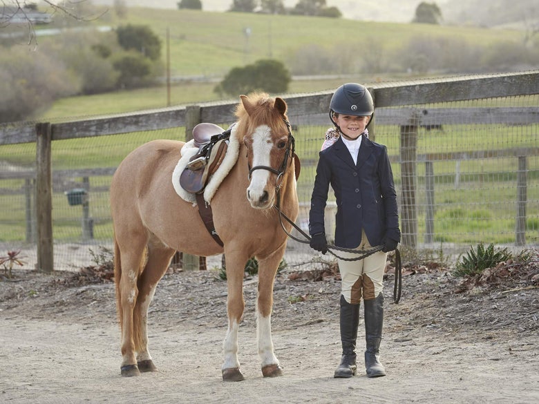 A young rider dressed in a show coat and tan breeches with her pony