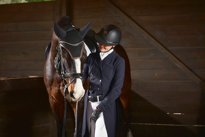 A dressage rider in proper dressage attire standing with her dark bay horse.