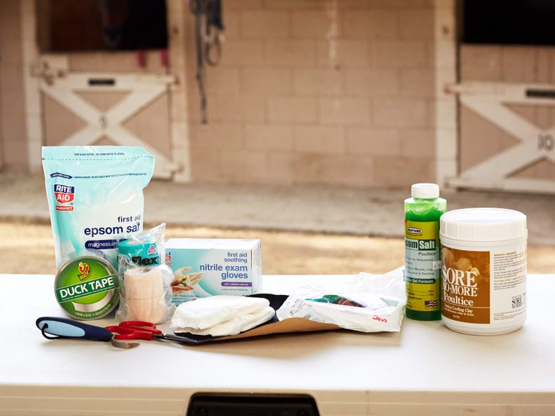 A variety of supplies for bandaging or wrapping a horse's hoof on a plastic table with a horse barn in the background. 