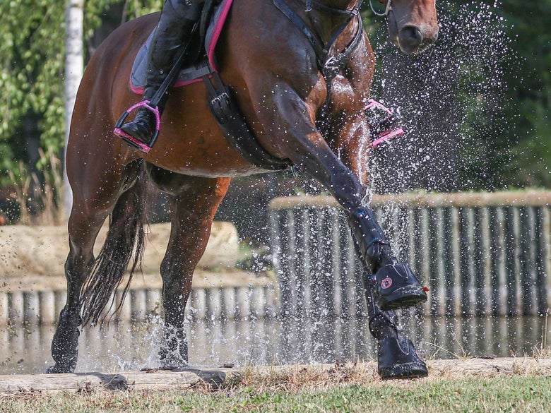 Rider cantering horse away from jump, with Equine Fusion hoof boots on.