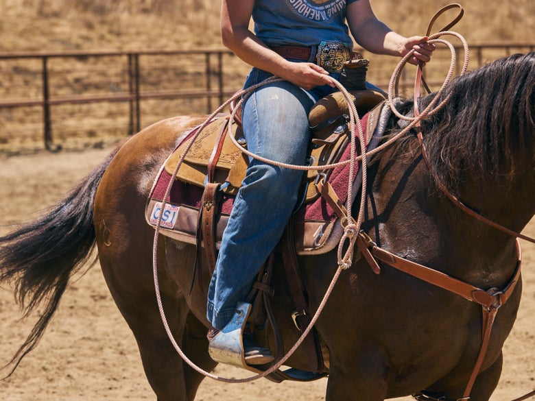 A rider holding the Fast Back Athena Breakaway rope while riding a bay horse.