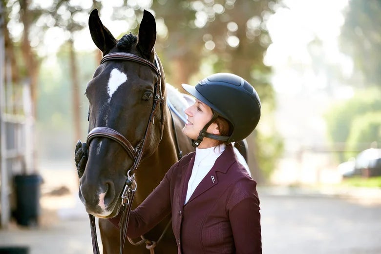 Hunter/Jumper rider standing next to her tacked up horse. 