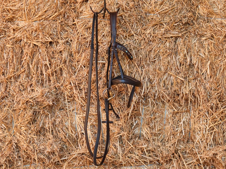 The ThinLine Classic Wrapped English Reins on a bridle hanging on a stack of straw bales.