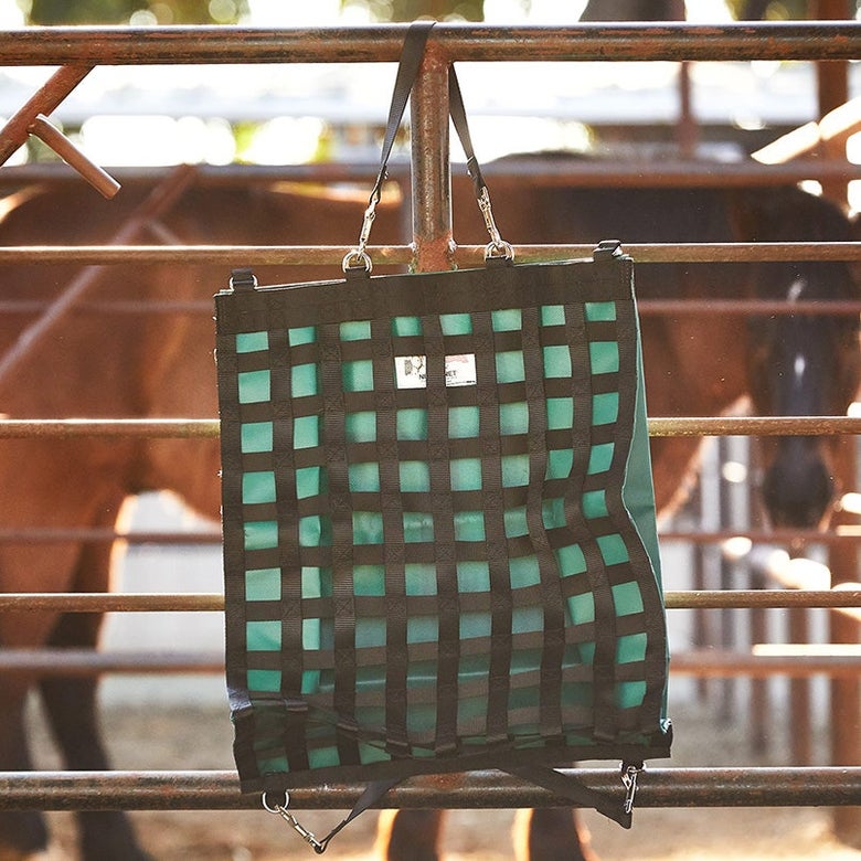 The NibbleNet Slow Feeder Hay Bay in Green handing on a gate.