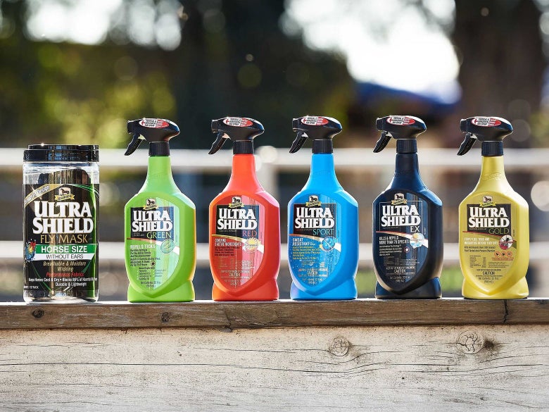 An assortment of Ultra Shield fly sprays and a fly mask by Absorbine for horses, all aligned on top of a fence