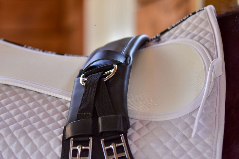 The ThinLine Short Dressage Girth resting on top of a white saddle pad.