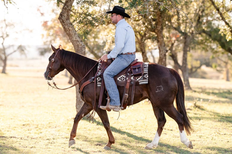 Man riding a horse in a western saddle through the trees. 