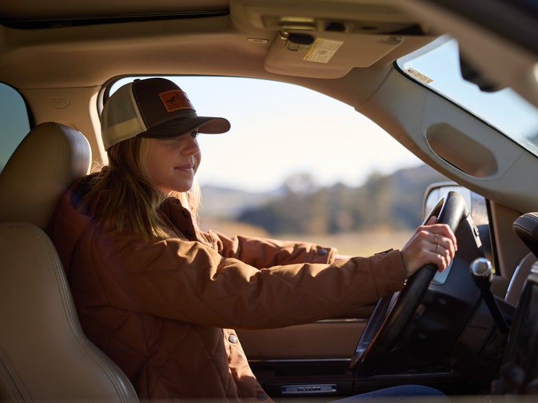 A woman wearing a Riding Warehouse hat driving her truck hauling a horse trailer.