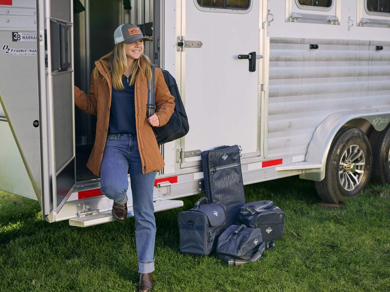 A woman standing outside her horse trailer tack room with packed LeMieux luggage bags outside waiting to be loaded.