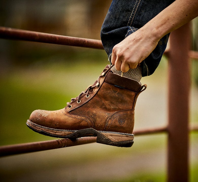 Person lacing up the Ariat Women's Anthem Round Toe H2O Lacer Boots with their foot against a fence.