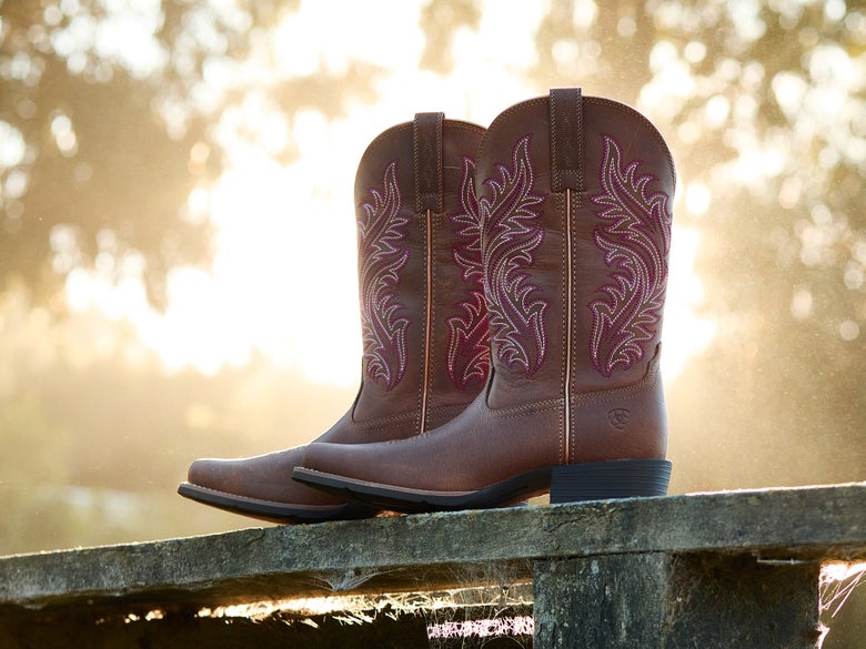 Ariat Round Up Narrow Cutter Toe Cowboy Boots sitting on a wooden fence rail.