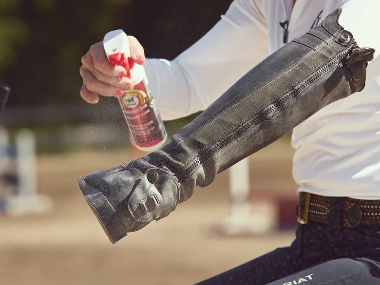 Woman showing the second step of cleaning a tall boot with using a leather spray from a few inches away.