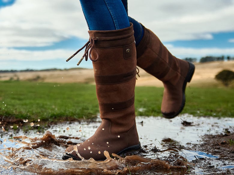 Someone wearing the Dublin River IV Women's Tall Boots while walking through a puddle.