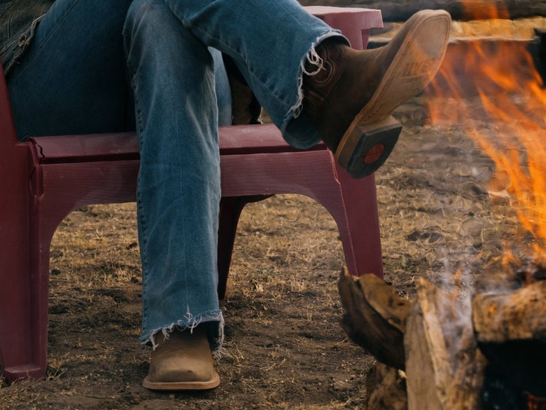 A cowgirl sitting by a campfire wearing the HYER Lola WesTrail Boots.
