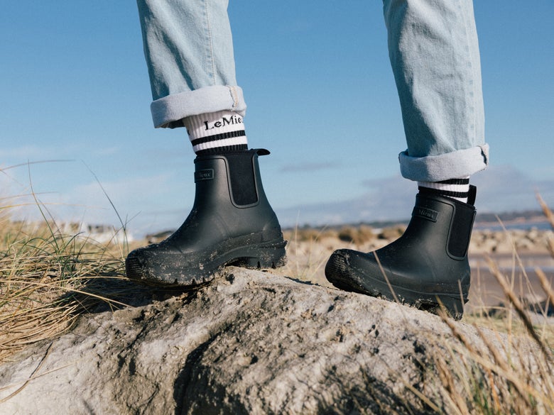 A woman walking in the LeMieux Bramshaw Chelsea Welly Muck Boots with the beach in the background. 