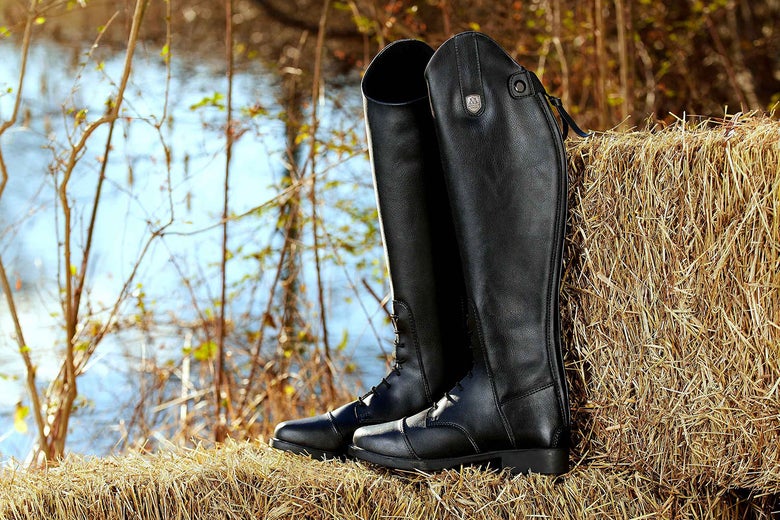 The Mountain Horse Kid's Veganza Tall Field Boots sitting on top of a hay bale. 
