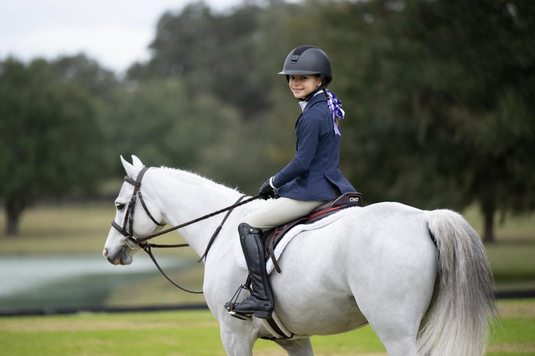 Girl wearing the Kerrits Crossover Tights in tan, riding a white pony.