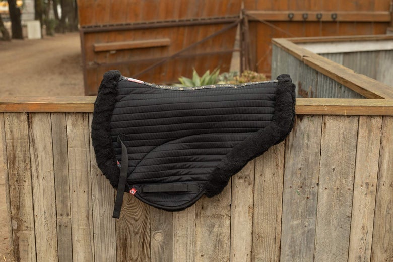 A Toklat T3 Endurance Coolback Saddle Pad sitting on top of a wooden fence. 