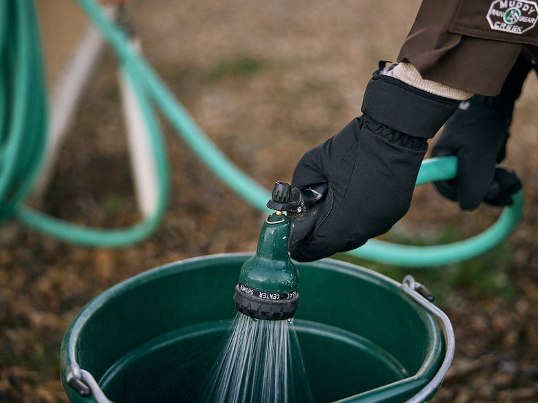 The Mountain Horse Heat Waterproof Winter Gloves being worn while filling a water bucket with a hose.