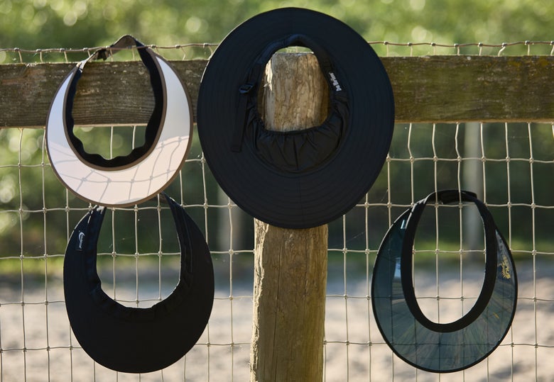 Assorted horseback riding helmet visors hanging on a fence.