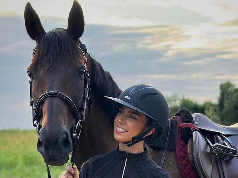 A rider wearing the IRH F1 Wide Brim Helmet, standing next to her horse.