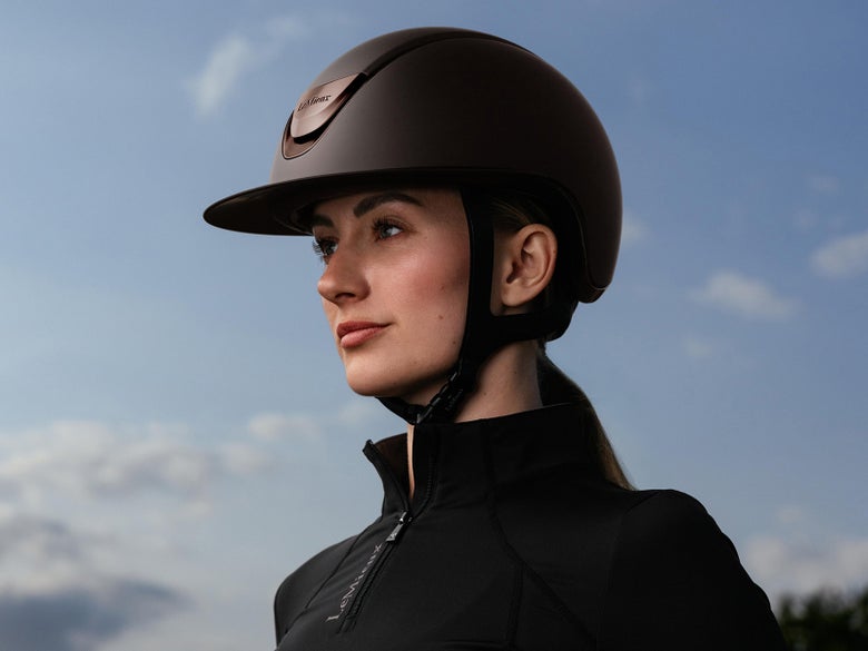 A woman wearing a LeMieux Verv Competition Helmet with a sunset in the background.