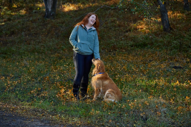 Woman standing on a hillside petting her golden retriever while wearing the LeMieux Phoebe Waterproof Anorak Jacket.
