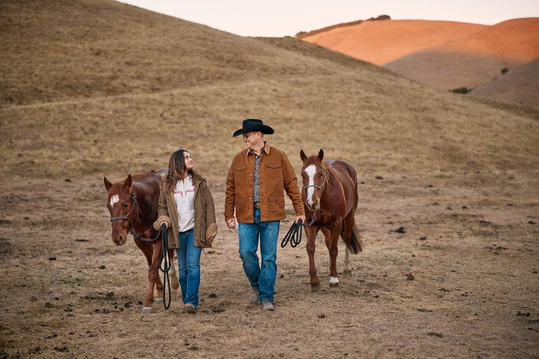 Man and women walking down a hill, leading two horses.