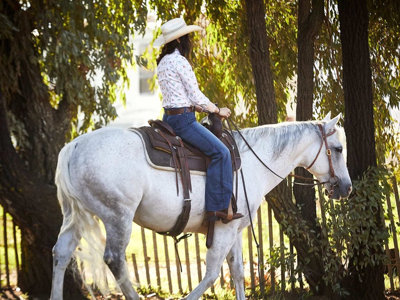 Lady riding her white horse wearing riding jeans and western tack