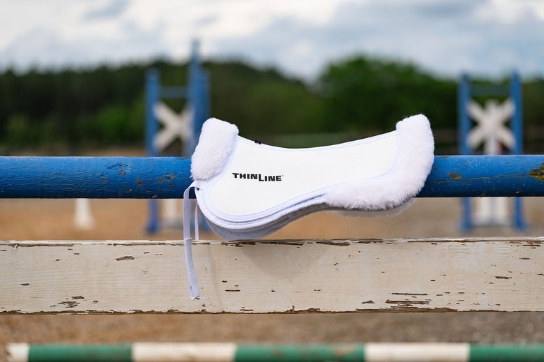 The ThinLine Sheepskin Rolled Trifecta Half Pad sittin on a fence rail.