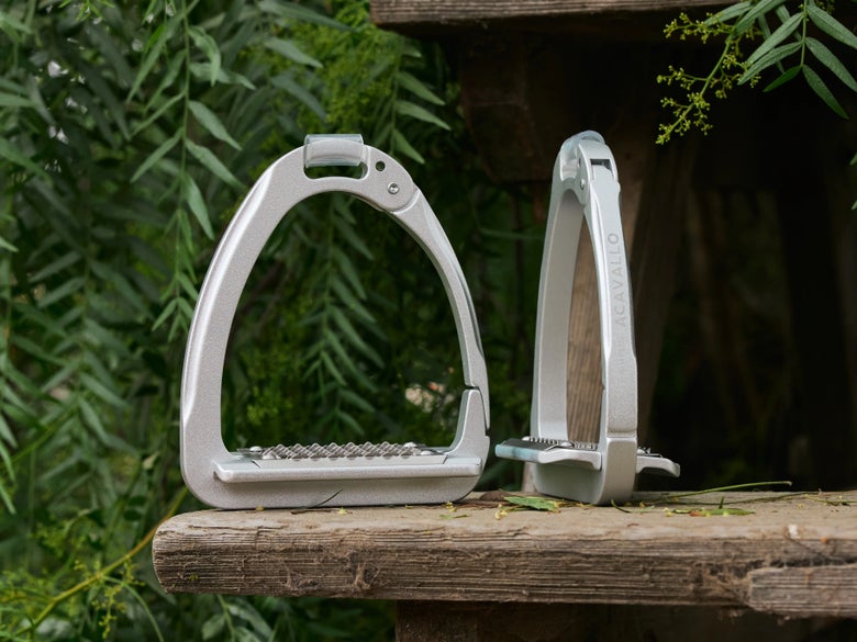 The Acavallo Arena stirrups on a wood board with foliage in the background.