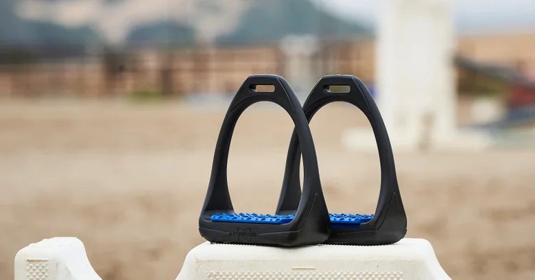 Black Compositi English Stirrups with a blue footbed sitting on a jump. 